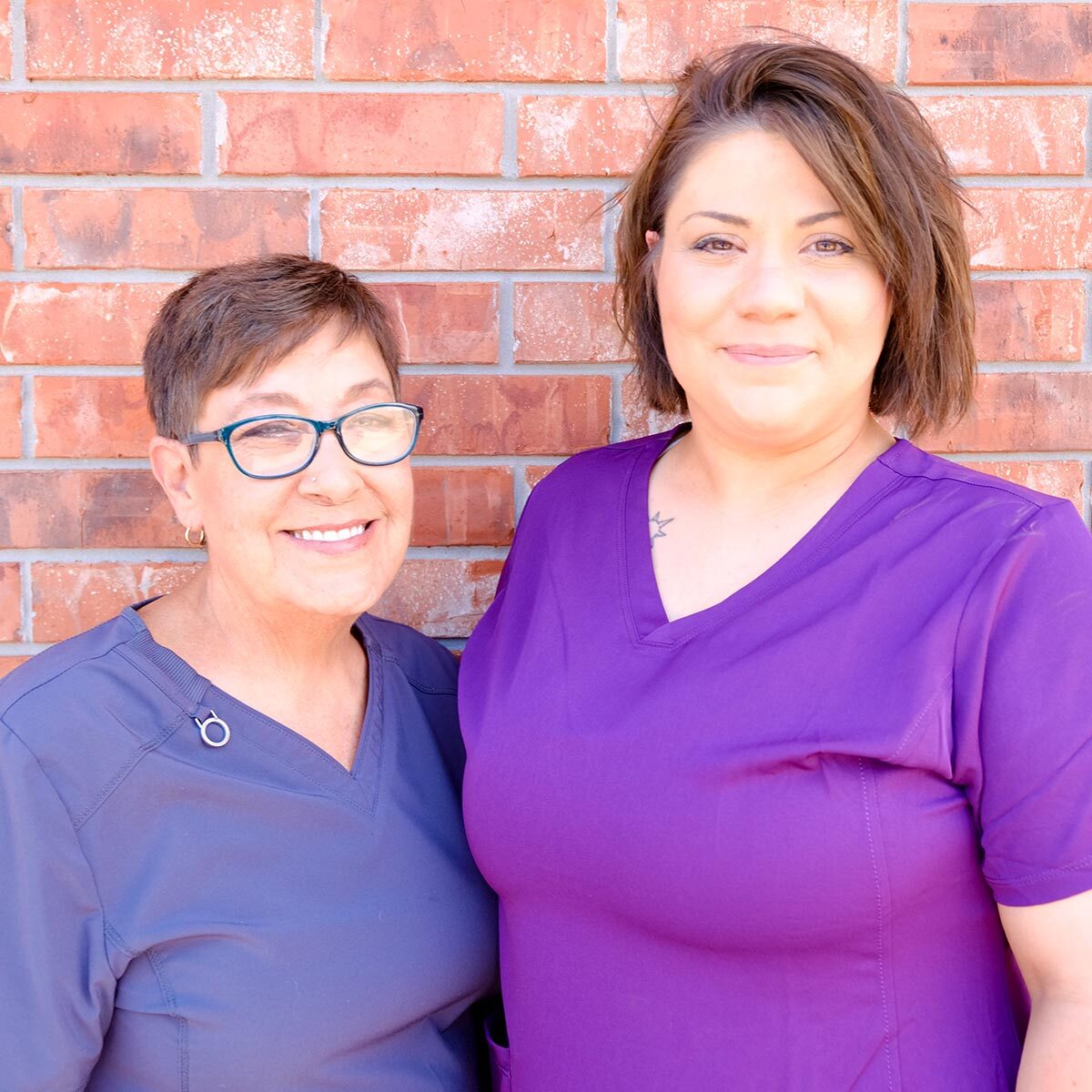 two female staff members smiling and posing outside in front of brick wall